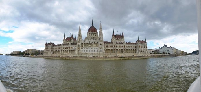 Hungarian Parliament Building viewed from Danube River showing Gothic Revival architecture with central dome and multiple spires under cloudy sky