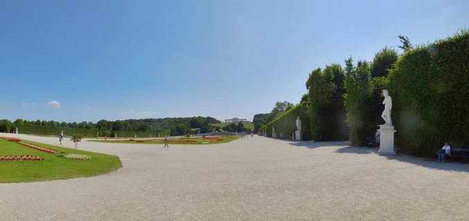 Yellow Baroque Schönbrunn Palace with formal gardens, flower beds, gravel paths, and visitors under blue sky in Vienna