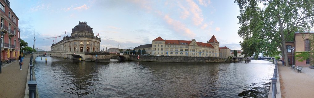 Panoramic view of the Bode Museum dome and historic buildings on Museum Island surrounded by the Spree River in Berlin at dusk with the TV tower in the distance