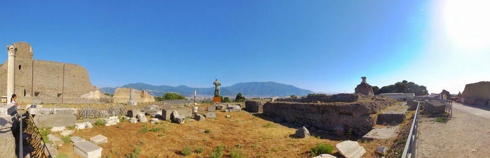 Panoramic view of ancient Roman stone ruins at Pompeii archaeological site with Mount Vesuvius mountain visible in the background under clear blue sky