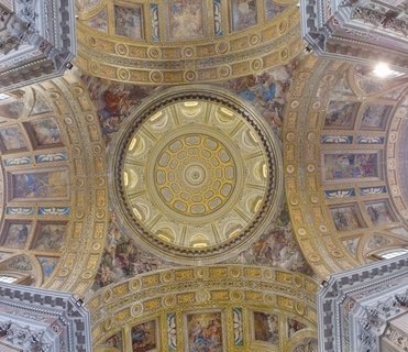 Interior view of ornate baroque cathedral with golden frescoed ceiling, marble columns, wooden pews, and elaborate altar in Naples, Italy