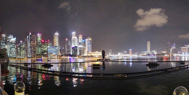 Night panoramic view of Singapore's illuminated Marina Bay skyline with skyscrapers, Merlion statue, and light reflections on water