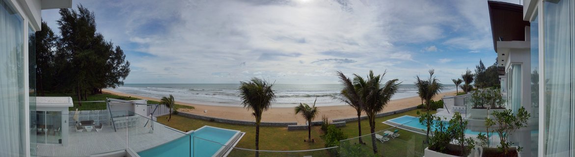Panoramic view of a luxury beachfront villa with two swimming pools, palm trees, sandy beach, and ocean in Phuket, Thailand