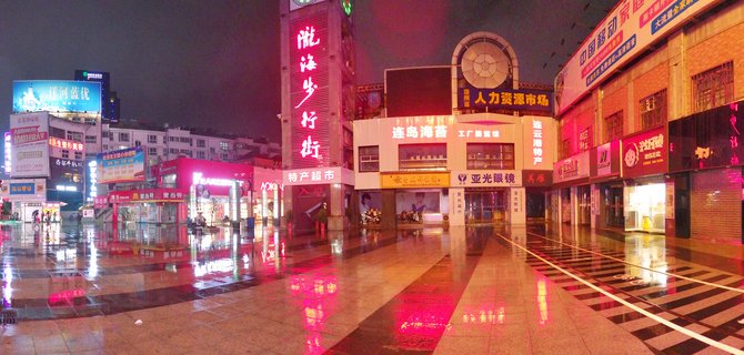 Night view of a Chinese pedestrian shopping street with bright neon signs in red and blue reflecting on wet pavement, buildings with Chinese text signage, crosswalk markings visible on the ground