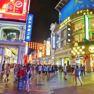 Busy pedestrian shopping street at night in Guangzhou with crowds of people walking beneath illuminated signs, McDonald's logo, and hanging red lanterns