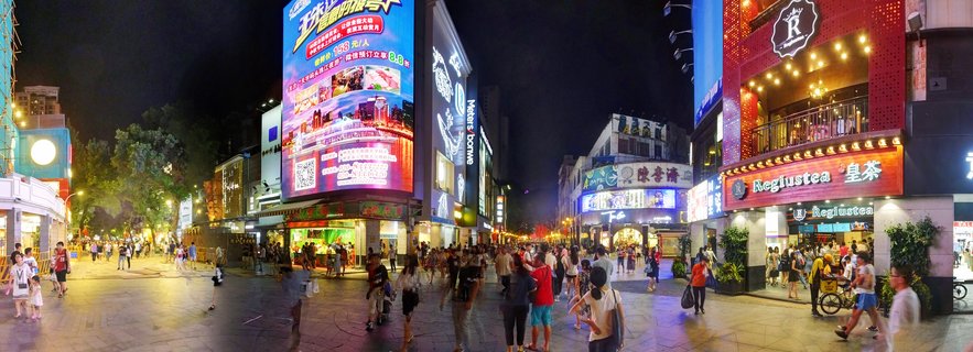 Wide nighttime view of a crowded pedestrian shopping street in Guangzhou with illuminated billboards, neon storefront signs, and people walking on paved walkway