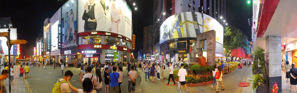 Crowded pedestrian shopping street at night in Guangzhou with large illuminated billboards, neon signs, and people walking between modern commercial buildings