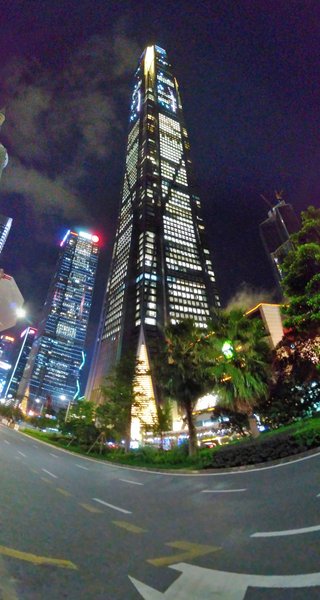 The Ping An Finance Center dominates Shenzhen's Futian District skyline at night, its illuminated facade rising above surrounding skyscrapers and palm-lined streets.