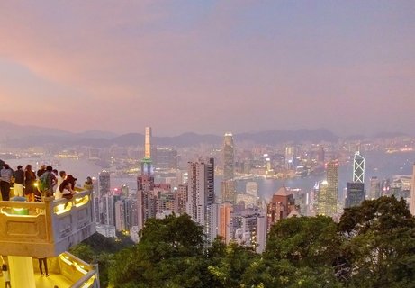 Panoramic view of Hong Kong skyline at dusk from Victoria Peak showing illuminated skyscrapers, Victoria Harbour, and tourists on an observation deck