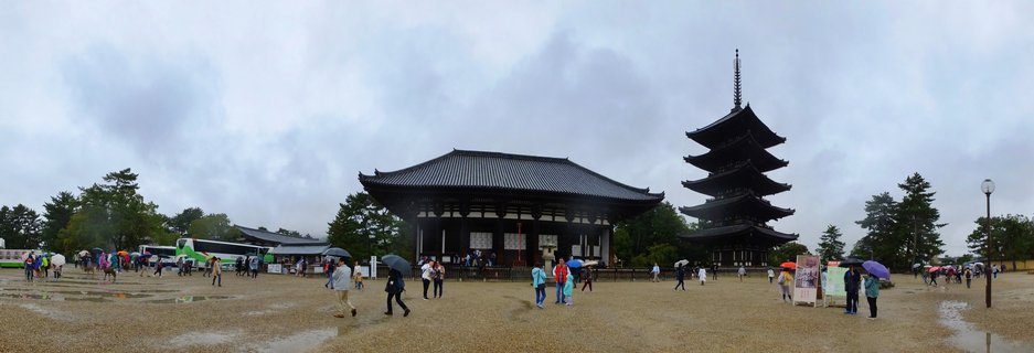 Wide view of To-ji Temple in Kyoto showing a five-story pagoda and main hall with visitors holding umbrellas on a rainy day