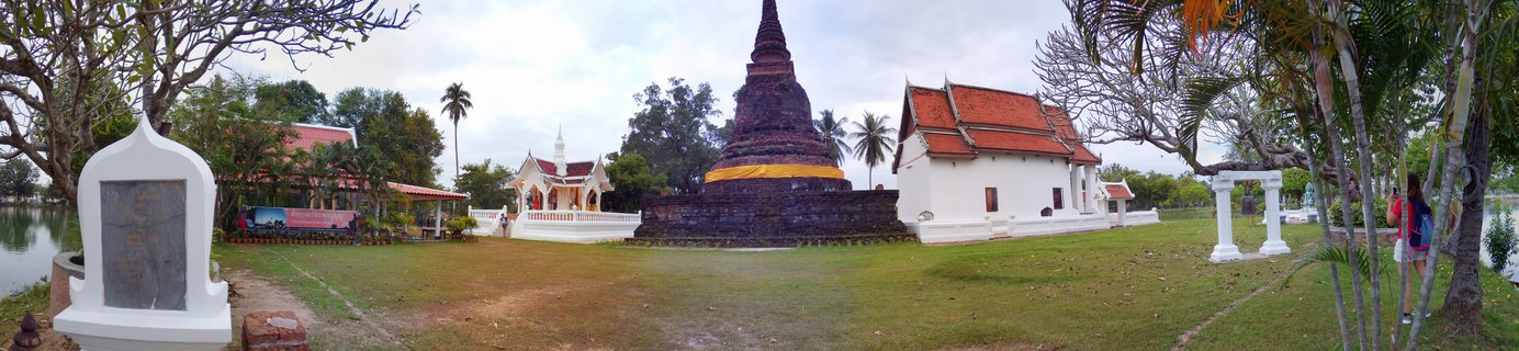 Ancient brick Buddhist stupa with golden ceremonial cloth at Thai temple complex with traditional buildings, Sukhothai Historical Park, Thailand