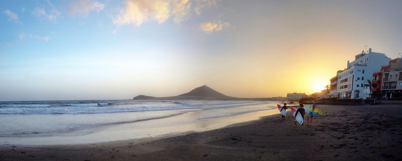 Surfers walking on El Médano beach at sunset with Montaña Roja volcanic mountain, Tenerife, Canary Islands, Spain