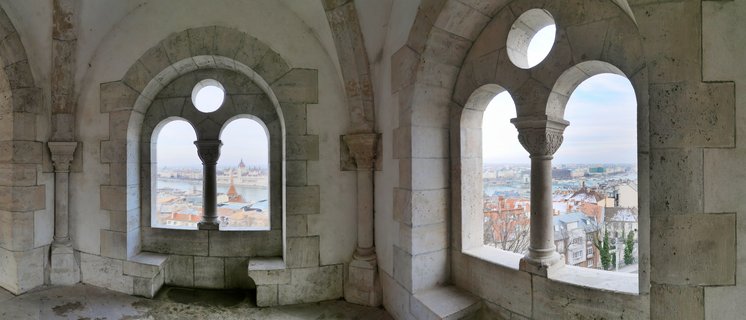 Stone arched windows with decorative columns at Fisherman's Bastion overlooking Budapest cityscape with Parliament Building visible through the openings
