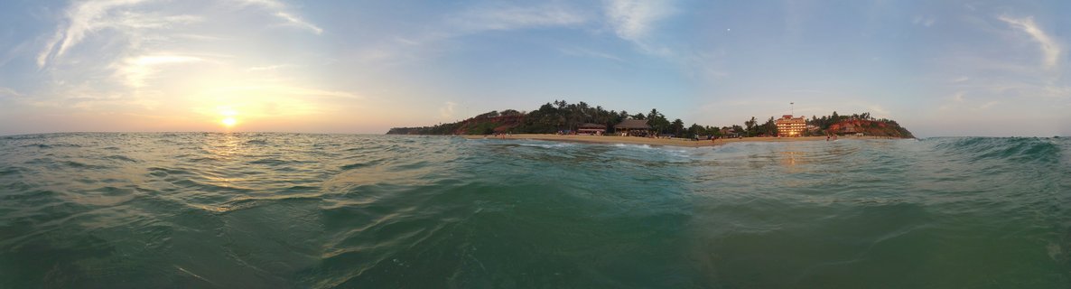 Panoramic seascape showing sunset over Arabian Sea with Varkala cliff, beach, resorts, and palm trees visible from water level
