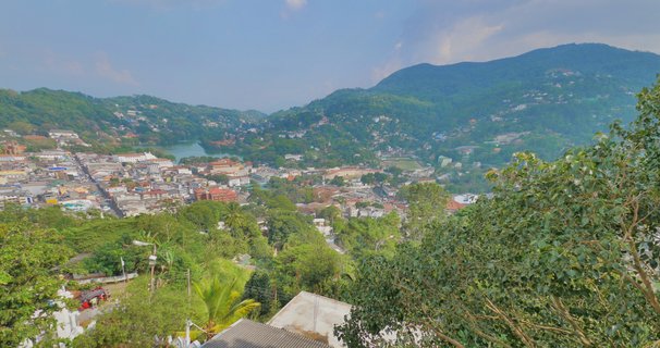 Panoramic view of Kandy city in Sri Lanka showing urban buildings, a lake, and surrounding green mountains covered in tropical vegetation