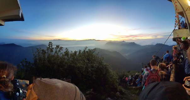 Crowd of pilgrims and tourists at mountain viewpoint watching sunrise over misty valley and layered mountain ranges at Sri Pada in Sri Lanka during dawn