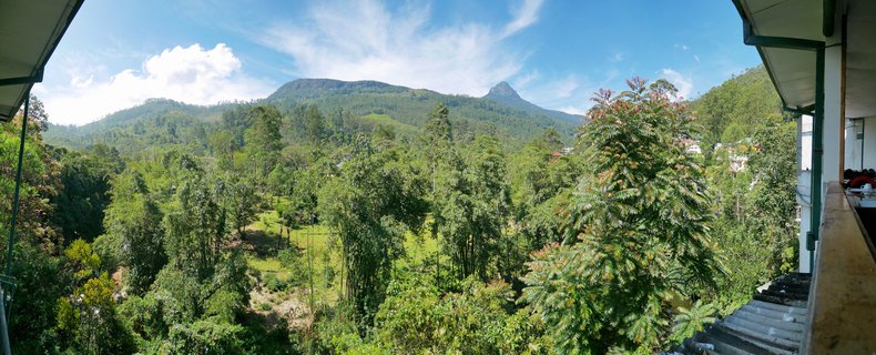 Panoramic view of forested mountains in Sri Lanka with blue sky and white clouds, viewed from a covered balcony structure