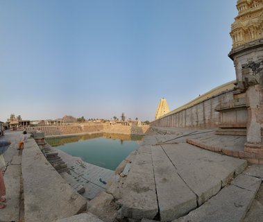 Ancient stone temple complex with sacred rectangular water tank, gopuram towers, and clear blue sky at Hampi, India