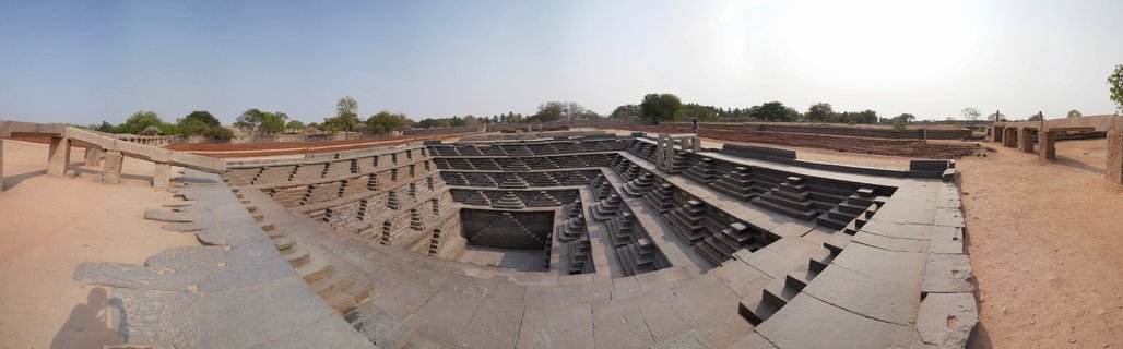 Aerial view of ancient stone stepped tank with geometric descending steps forming rectangular pattern under clear blue sky at Hampi ruins India