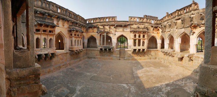 Historic stone courtyard with multiple pointed arches and colonnades surrounding an open paved area at Hampi heritage site in India