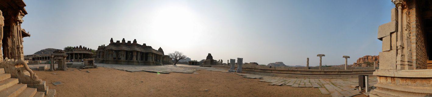 Panoramic view of ancient stone temple ruins with carved pillars, columns, and courtyard structures at Hampi heritage site in Karnataka, India under bright afternoon sunlight
