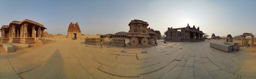 Ancient stone chariot structure with carved wheels at Vittala Temple complex in Hampi, India, surrounded by pillared halls and temple ruins under clear sky