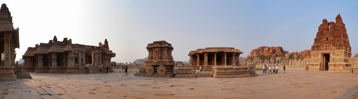 Ancient stone chariot monument in courtyard of Vittala Temple complex with Hindu temple structures and rocky hills at Hampi, India