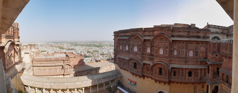 Red sandstone fort buildings with arched windows and balconies overlooking a city with blue-painted houses under clear sky