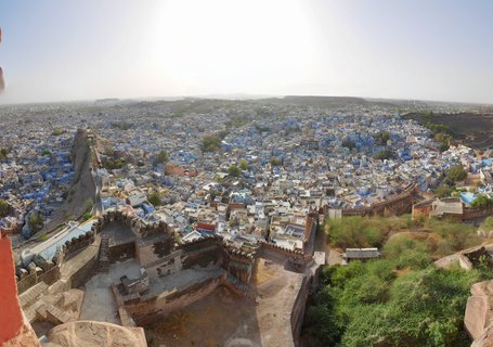 Panoramic aerial view of Jodhpur city showing blue-painted buildings, ancient fort walls in foreground, and arid landscape extending to horizon under bright sky