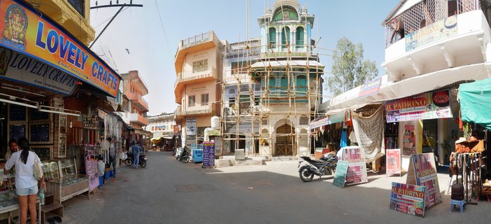 Street view of Pushkar market with colorful shop signs, traditional Indian buildings, motorcycles, and pedestrians under clear blue sky