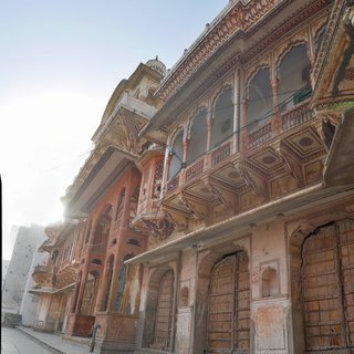 Street view of traditional multi-story haveli buildings in Pushkar with ornate carved balconies, painted frescoes, arched wooden doors, and weathered facades in warm earth tones