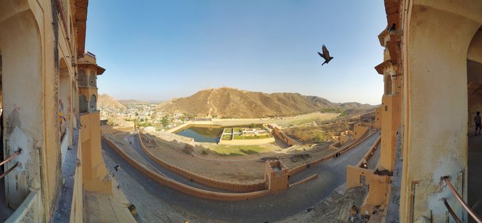 Panoramic view from Amber Fort corridor showing Maota Lake, Mughal garden, and Aravalli Hills in Jaipur, India with a bird flying across blue sky