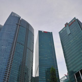 Three tall glass skyscrapers photographed from below showing UBS and NTUC company logos at the top against a cloudy sky