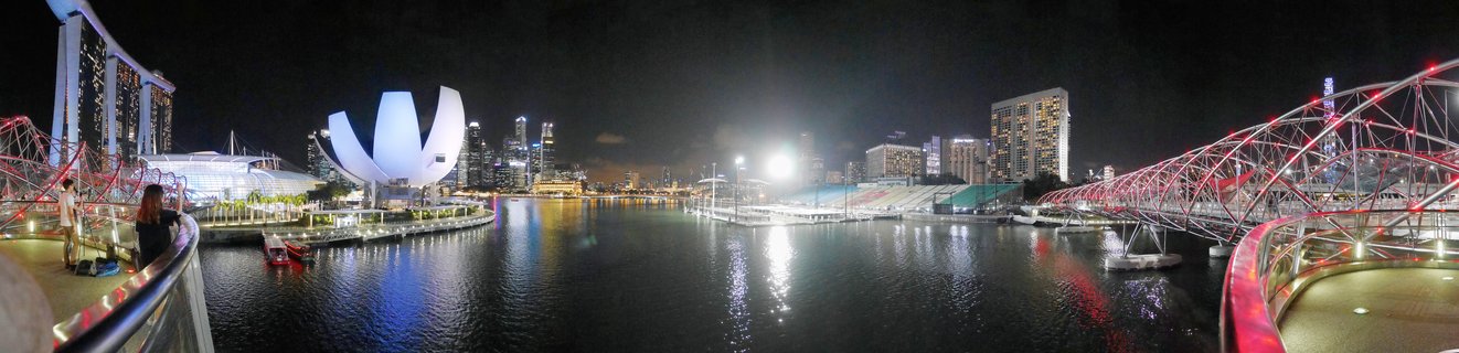 Panoramic night photograph of Singapore Marina Bay showing illuminated Marina Bay Sands hotel, ArtScience Museum, Helix Bridge, and city skyline with water reflections