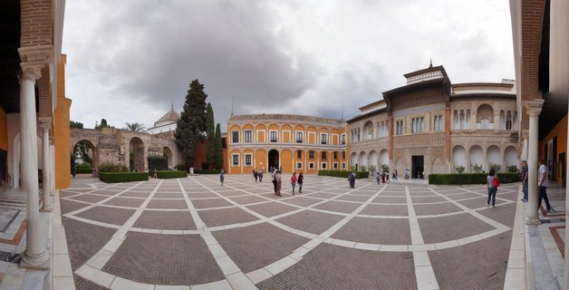Wide courtyard with geometric patterned stone paving surrounded by orange and cream buildings with Moorish arches and columns at the Real Alcázar palace in Seville