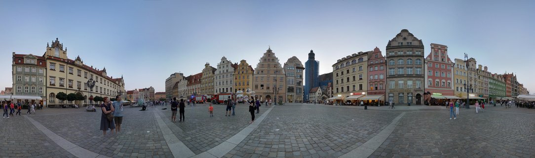 Panoramic view of Wrocław Market Square showing colorful historic buildings with gabled facades surrounding a cobblestone plaza with pedestrians at dusk