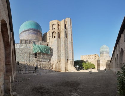 Historic Islamic mausoleums with large turquoise domes and ornate blue tilework at Shah-i-Zinda necropolis in Samarkand, with scaffolding on one building and clear blue sky above