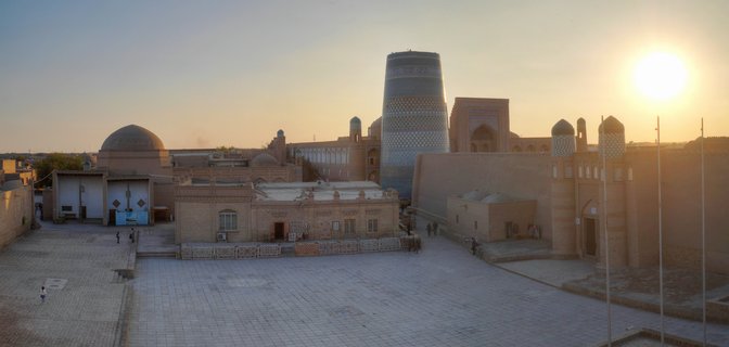 Aerial panoramic view of Kalta Minor minaret and domed Islamic buildings within Itchan Kala fortress walls during golden hour sunset in Khiva, Uzbekistan