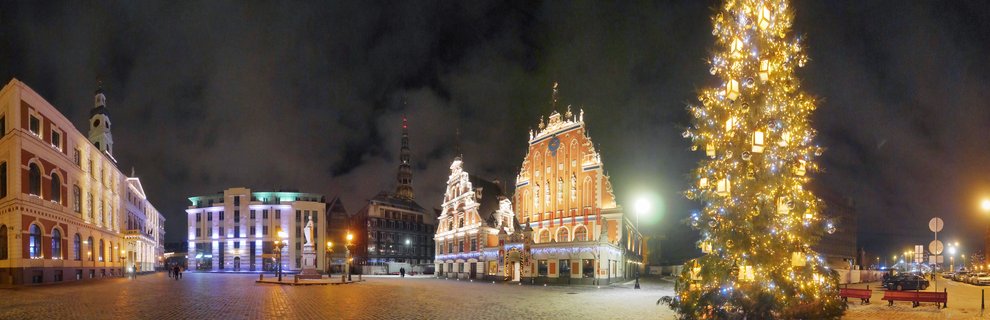 Night view of Riga Town Hall Square with illuminated historic buildings including the House of the Blackheads and a large decorated Christmas tree on cobblestone plaza
