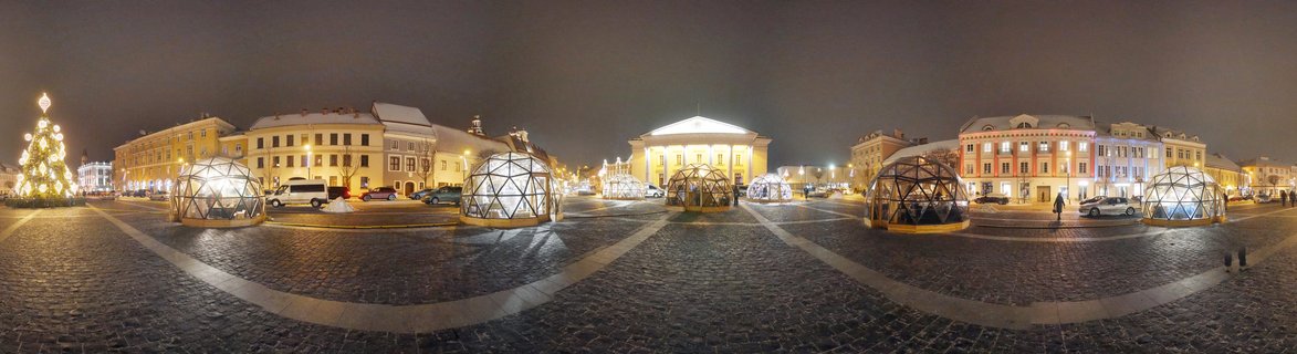 Night panoramic view of Cathedral Square in Vilnius, Lithuania showing illuminated Christmas tree, geodesic dome structures, cobblestone plaza, and historic buildings with snow on rooftops