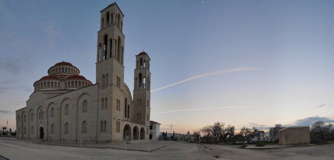 Large Orthodox church with two bell towers and red domes on a paved plaza under twilight sky with moon visible