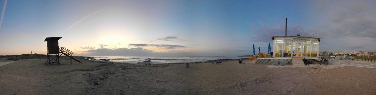 Panoramic beach scene at sunset showing a wooden lifeguard tower and illuminated beach cafe on the Mediterranean coast in Paphos, Cyprus