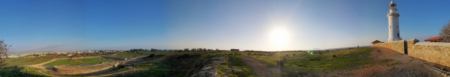 White lighthouse on coastal cliff overlooking ancient archaeological ruins and Mediterranean landscape under clear blue sky in Paphos, Cyprus