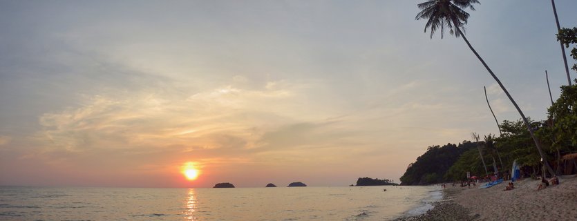 Sunset over Gulf of Thailand at Koh Chang beach with palm trees and distant islands
