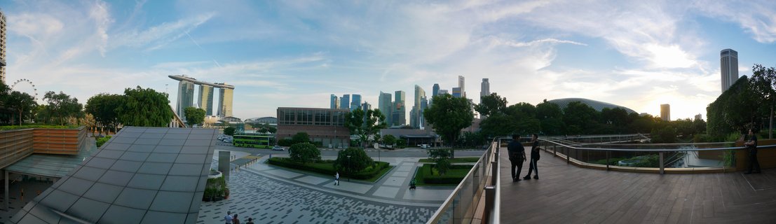 Wide panoramic photograph of Singapore's Marina Bay showing Marina Bay Sands hotel, downtown skyscrapers, and the Esplanade theatre under a blue sky with scattered clouds during late afternoon