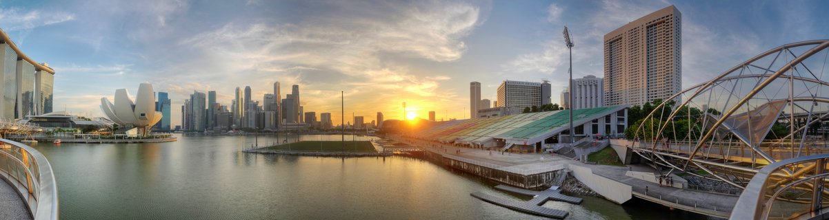 Panoramic cityscape of Singapore Marina Bay at sunset showing Marina Bay Sands hotel, ArtScience Museum, Helix Bridge, and downtown skyscrapers reflected in water