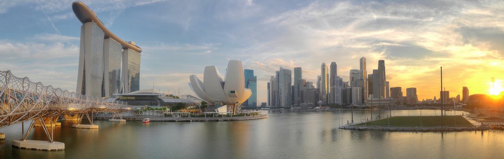 Panoramic view of Singapore Marina Bay at sunset showing Marina Bay Sands hotel, ArtScience Museum, Helix Bridge, and downtown skyscrapers reflected in water