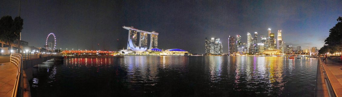 Night panoramic view of Singapore Marina Bay showing illuminated Marina Bay Sands hotel, Singapore Flyer Ferris wheel, ArtScience Museum, and downtown skyscrapers reflected in water