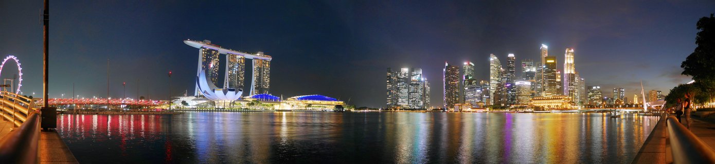 Night panoramic view of Singapore's Marina Bay showing illuminated Marina Bay Sands hotel, Singapore Flyer wheel, and CBD skyscrapers with reflections in water