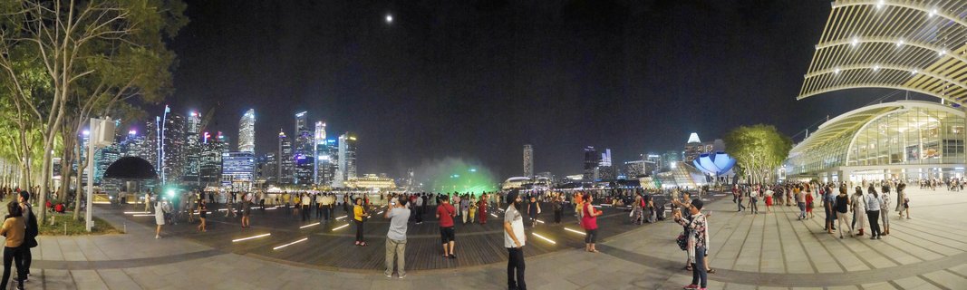 Night panoramic view of Singapore's Marina Bay with illuminated skyscrapers, ArtScience Museum, and crowds of people on the waterfront promenade
